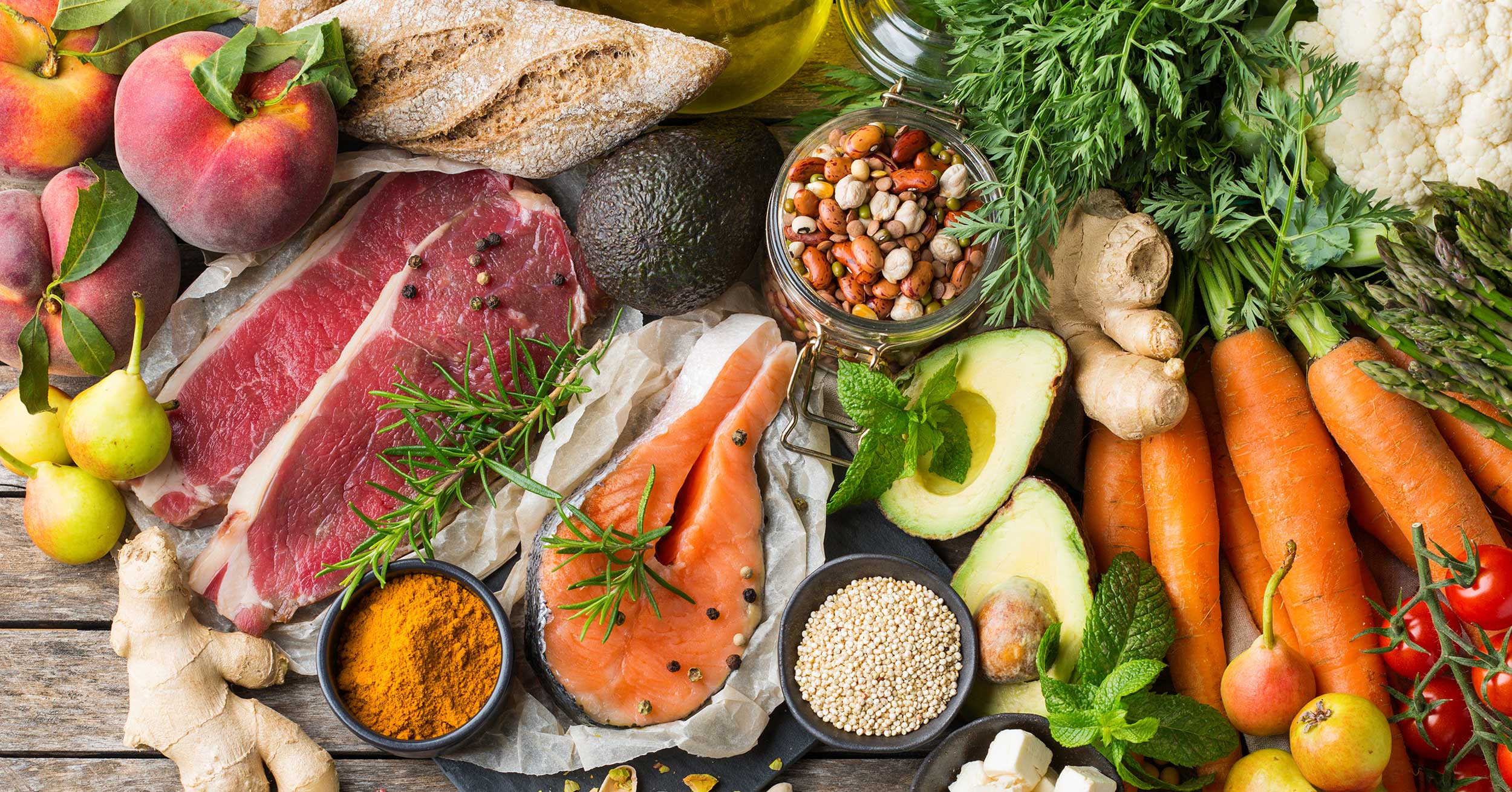 Auswahl an gesunden Lebensmitteln zum Kochen auf einem Küchentisch. Ansicht von oben flach gelegter Hintergrund. Beinhaltet Gemüse, Obst, proteinreiches Fleisch, Nüsse, Käse.